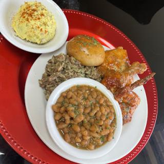 A delicious plate featuring shrimp, rice, a biscuit, and a savory bean dish.