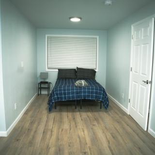 A small, minimalist bedroom with blue bedding and a wooden floor.