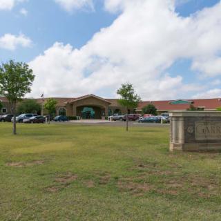 A school building with a grassy front lawn and a parking lot under a partly cloudy sky.