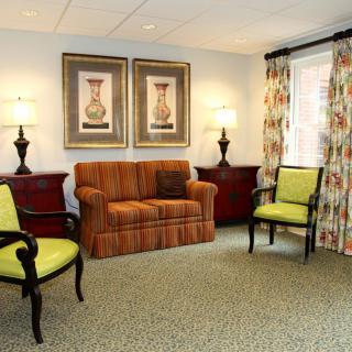 A cozy living room with a sofa, two green chairs, and decorative lamps beside framed artwork.