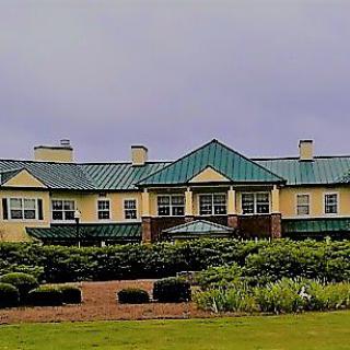 A large building with a green roof surrounded by well-maintained shrubs under a cloudy sky.