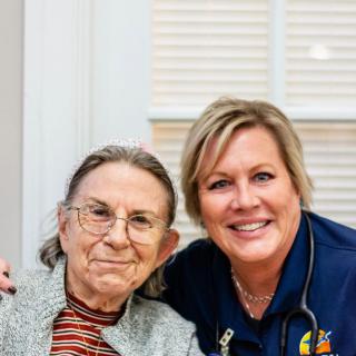 An elderly woman posing with a healthcare worker, both smiling warmly.