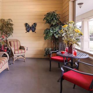 A cozy indoor patio area with wicker and upholstered furniture, accented by vibrant red cushions, decorative plants, and butterfly wall art.