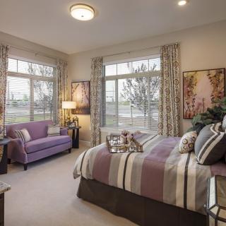 A cozy bedroom with a striped bedspread, sofa, and large windows allowing natural light.
