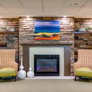 A cozy living room with a stone fireplace, two chairs, and colorful artwork above.