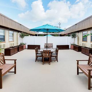 A spacious outdoor patio with wooden furniture and a blue umbrella under a clear sky.