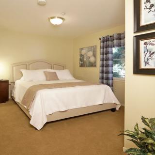 A cozy bedroom with a neatly made bed, framed art on the walls, and a window with plaid curtains.