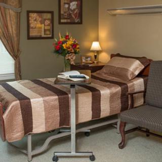 A well-furnished hospital room with a bed, bedside table, and a chair.