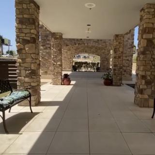 A covered walkway with stone columns and benches, providing a shaded outdoor space.