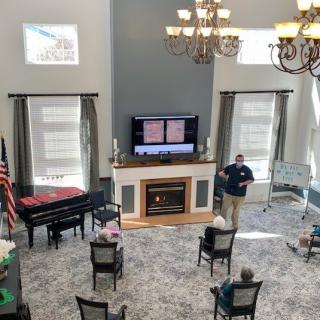 A spacious room with a television, fireplace, and piano, where several people are seated for an event.