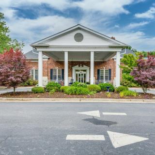 A symmetrical brick building with white columns and a landscaped entrance under a partly cloudy sky.