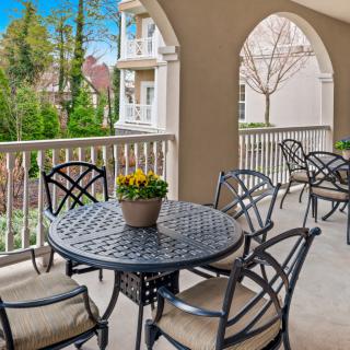 A cozy balcony with outdoor furniture and a potted plant, overlooking lush greenery and nearby buildings.