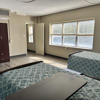 A well-lit bedroom featuring two beds and large windows.
