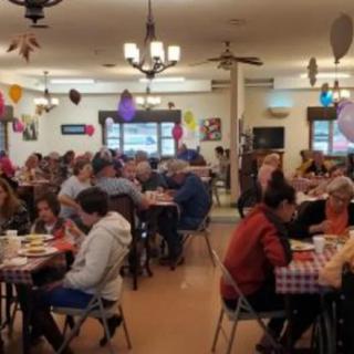 A lively community gathering with people enjoying a meal in a decorated indoor space.