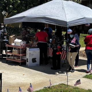 A community gathering under a tent, with people wearing masks and celebrating around American flags.