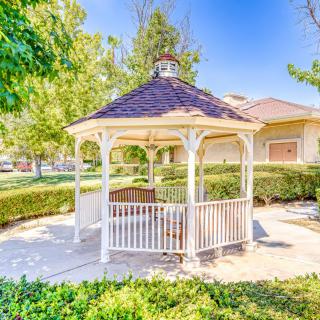 A charming gazebo in a sunny garden setting, surrounded by trees and greenery.