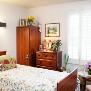 A cozy bedroom with wooden furniture, floral bedding, and various plants adorning the dresser.