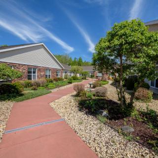 A well-maintained garden with a stone path leading past buildings under a bright blue sky.