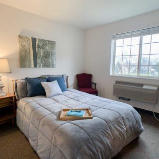 A cozy bedroom with a neatly made bed, artwork on the wall, and natural light streaming through the window.