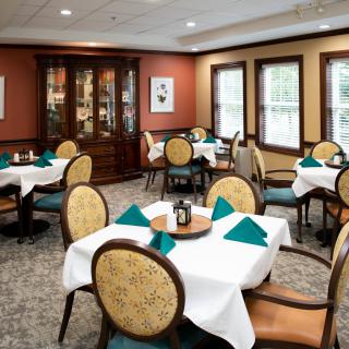 An elegant dining room with neatly arranged tables and chairs, featuring crisp white tablecloths and teal napkins.