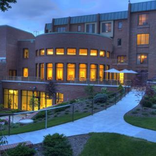 A well-lit brick building with large windows and a winding pathway in the evening.