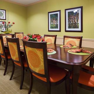 A warmly decorated dining room with a large table and chairs, featuring vibrant artwork on the walls.