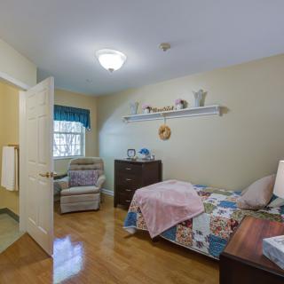 A cozy, well-furnished bedroom with a bed, dresser, and comfortable chair near the window.
