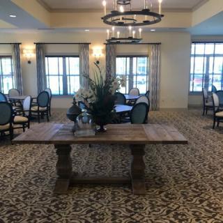 An elegant dining area with a central wooden table, surrounded by chairs, and illuminated by a chandelier.