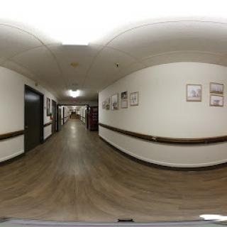 A wide-angle view of a well-lit hallway adorned with framed pictures along the walls.