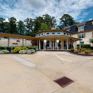 A modern building with a circular entrance and driveway, surrounded by trees and neatly arranged landscaping.