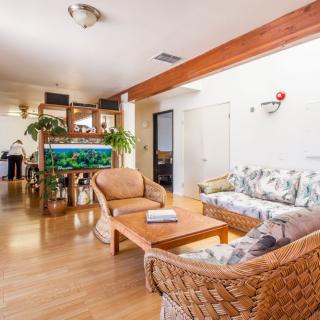 A cozy living room with wooden flooring, featuring a large aquarium, wicker furniture, and a floral-patterned sofa.