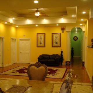 A warmly lit living room with yellow walls, featuring a sofa, artwork on the walls, and a decorative carpet.