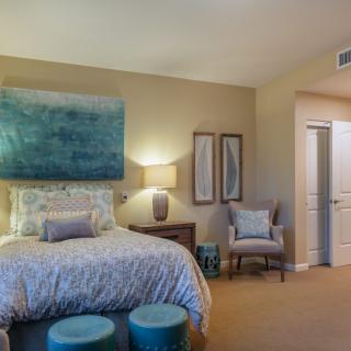 A cozy and well-decorated bedroom featuring a bed with a patterned comforter, artwork above the headboard, and elegant furnishings.