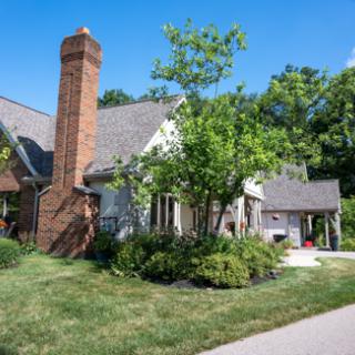 A charming residential home with a brick chimney and lush greenery surrounding it.