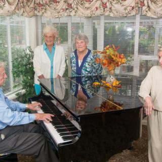 A group of elderly people gathered around a piano, enjoying music indoors.