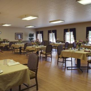 An empty dining room with neatly set tables and chairs, illuminated by natural light from the windows.