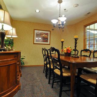 A warmly lit dining room featuring a large wooden table surrounded by chairs, with elegant lighting and decorative elements.