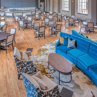 A spacious lounge area with a variety of seating options, including a blue sofa, chairs, and tables on a wooden floor.
