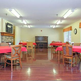 A spacious dining area with multiple tables covered in red tablecloths and wooden chairs arranged neatly on a hardwood floor.