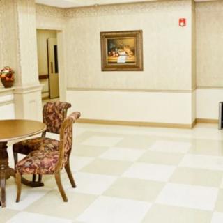 A spacious room with a table and chairs, featuring a painting on the wall and checkered floor tiles.