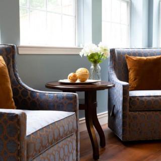 A cozy living room setup with two upholstered chairs, a wooden side table, and a vase of flowers by the window.