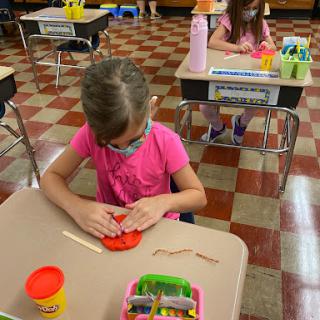 A child focused on a creative activity using playdough in a classroom setting.