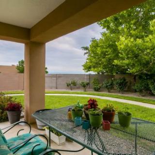 A cozy backyard patio with a metal table and chairs, surrounded by lush greenery and potted plants.