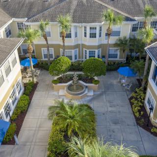 Aerial view of a courtyard with a fountain, surrounded by palm trees and residential buildings.