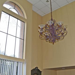 Elegant chandelier hanging in a room with high ceilings and large arched windows.
