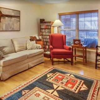 A cozy living room with a sofa, red armchair, patterned rug, and lamp by the window.
