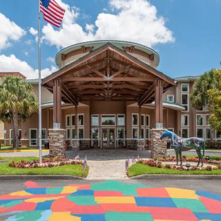 A building entrance featuring a wooden canopy, an American flag, horse sculpture, and colorful pavement.