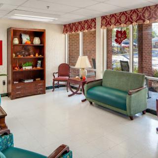 A cozy waiting room with green sofas, a bookshelf, and decorative items under window blinds.