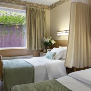 A cozy hotel room with two neatly made twin beds, complemented by elegant curtains and a view through the window.