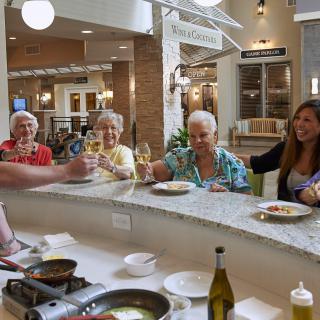 A group of seniors enjoying a meal and raising glasses in celebration at a kitchen counter.